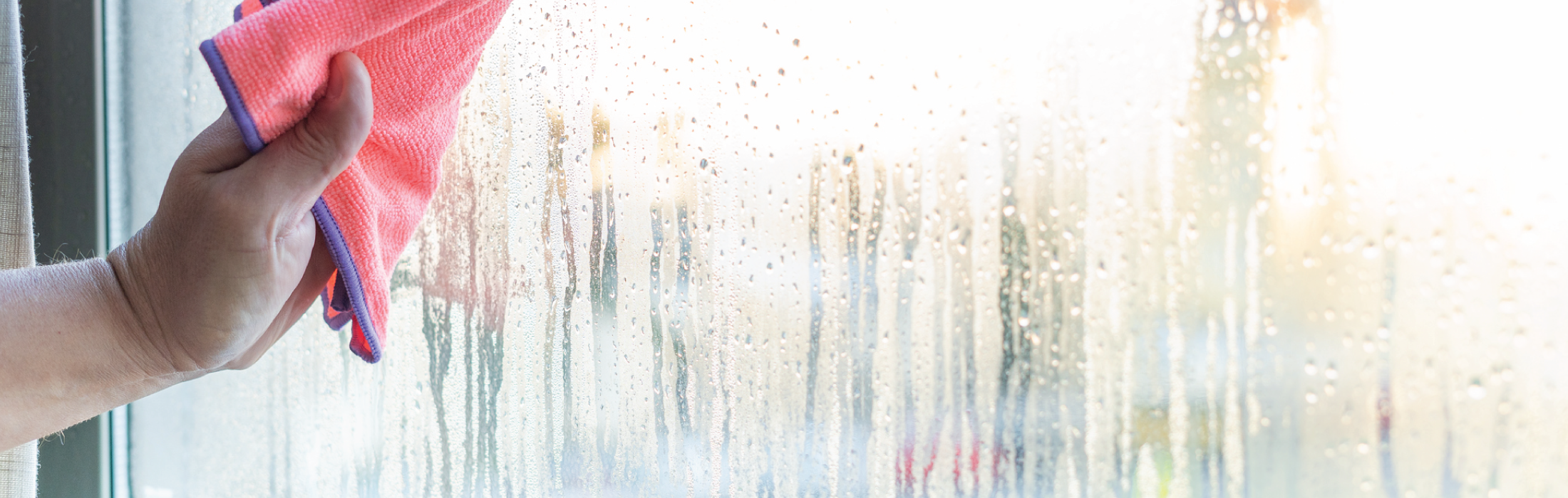 Photo of a person's hand wiping away water condensation from window