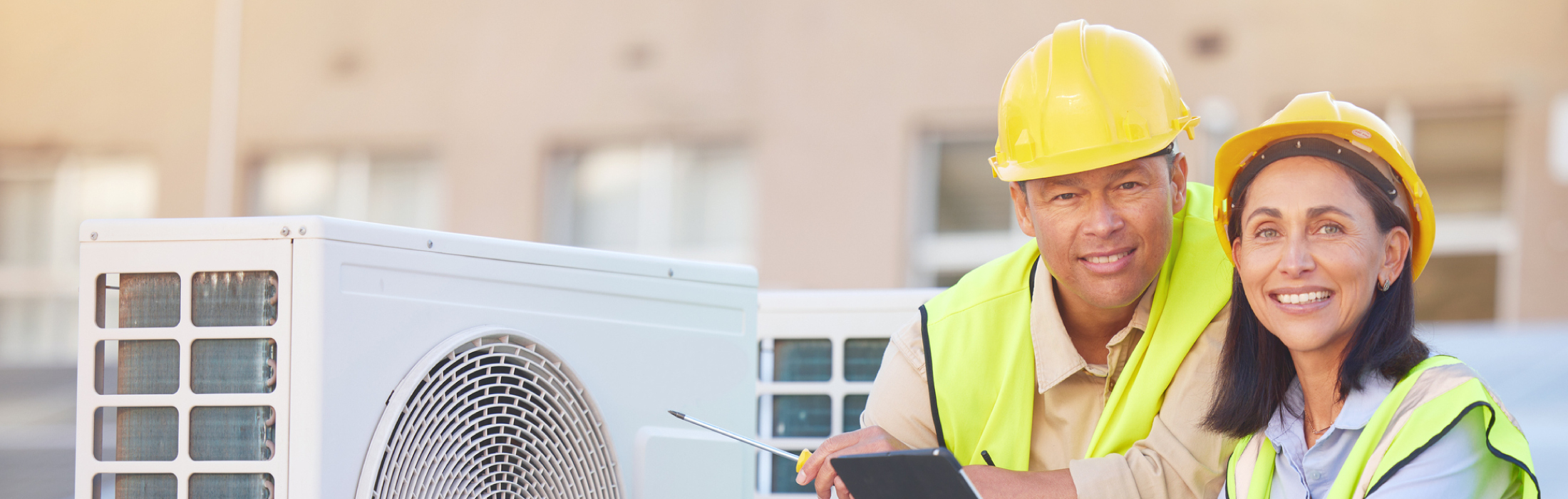 Man and woman in yellow hardhats installing a commercial HVAC system