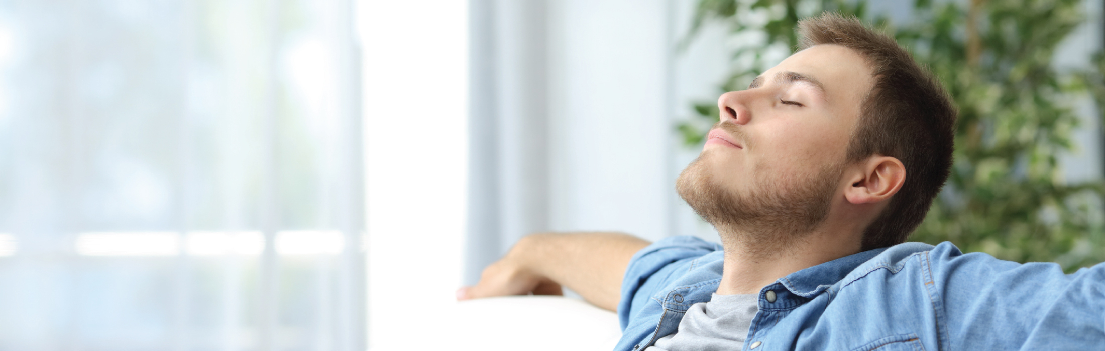 Man sitting on a couch in blue shirt enjoying purified air from HVAC filter/system